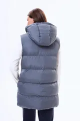 Chaleco puffer largo de color negro, con cierre frontal completo, capucha ajustable con cordones y bolsillos laterales. Diseño acolchado con costuras horizontales.