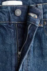 Jean de tiro alto con corte mom slim, confeccionado en denim azul oscuro con leve elasticidad. Presenta diseño de cinco bolsillos, cierre con botón y pierna recta que se estrecha ligeramente hacia el bajo.