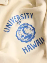 Buzo de media cierre y cuello polo color beige, con estampado azul en el pecho que dice "University of Hawaii" y manga larga.