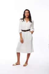 Vestido camisero blanco de poliéster con corte midi, cuello camisero, mangas largas con puños abotonados, cierre frontal con botones y cinturón marrón.