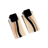 Par de aros colgantes con forma rectangular en color beige con líneas onduladas en negro, marrón y celeste. La parte superior es cuadrada y de color negro.