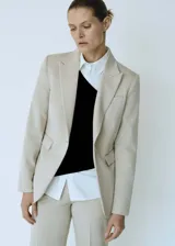 Blazer entallado de color beige con solapas de muesca, hombros estructurados y cierre frontal de un botón. Presenta bolsillos de ribete delanteros, pinzas de entalle y abertura posterior.