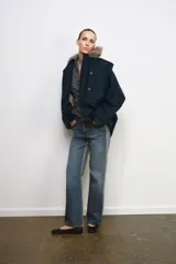 Trench corto de corte recto con capucha y cuello desmontable efecto pelo. Presenta cierre frontal con botones, bolsillos laterales y mangas largas con trabillas en los puños.