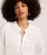 Blusa tipo bata de color celeste con mangas largas y cuello mao con lazo. Presenta detalles de bordado floral calado tipo laise en el frente y cierre parcial con botones.