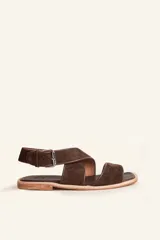 Sandalias planas de gamuza marrón con tiras cruzadas y tira ajustable al tobillo con hebilla metálica.