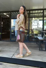 Bolso matera de cuero color marrón con doble asa de mano y correa larga desmontable. Incluye accesorio decorativo de borlas rosas y blancas.