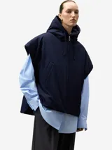 Chaleco acolchado de color azul marino, con capucha ajustable mediante cordón y cierre frontal de cremallera. Presenta bolsillos de vivo inclinados en el delantero y cierres laterales con broches a presión.