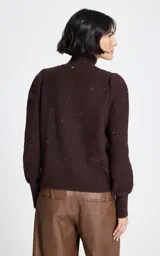 Polera de punto color marrón con cuello alto y mangas largas con puños ajustados. Presenta un sutil diseño de brillos dorados distribuidos por toda la prenda.