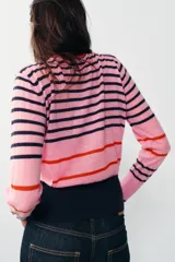 Jersey de punto de cuello redondo y manga larga con puños ajustados. Presenta un diseño de rayas horizontales en tonos rosa, azul marino y detalles en rojo.
