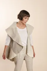 Chaleco sin mangas de tejido de lana fina sin teñir, con diseño circular y bloques de color beige y marrón. Presenta un cuello amplio y solapa que permite usarlo como chaleco largo o capa corta.
