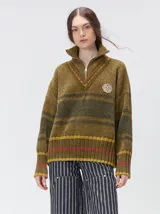 Pullover de punto con textura aterciopelada, diseño oversize, cuello polo con cierre frontal parcial y detalles de pespuntes en contraste. Presenta rayas horizontales en tonos tierra y un parche bordado con la letra M en el pecho.