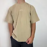 Remera color arena de corte oversize, con cuello redondo y mangas cortas. Presenta un pequeño bordado de un sol naciente en el centro del pecho.