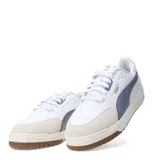 Championes urbanos Puma modelo Shuffle Downtown OG, de diseño retro con base blanca, detalles en gris azulado y puntera de gamuza en tono beige. Cuenta con suela de goma color caramelo y logo de la marca en dorado.