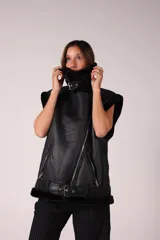 Chaleco negro de eco cuero con cuello y borde de gamulan. Tiene cierre cruzado con cremallera y cinturón con hebilla en la cintura.