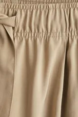 Pantalón color beige de corte amplio, con cintura elástica y lazo para atar. Confeccionado en sarga de mezcla de modal, con bolsillos laterales y un bolsillo decorativo atrás.