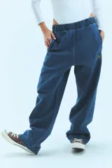 Pantalón de jean azul de corte babucha, tiro medio, con elástico en la cintura, bolsillos delanteros y logo bordado en amarillo en la pierna derecha.