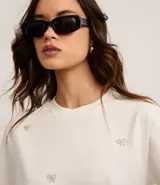 Blusa color crudo de algodón con cuello redondo y mangas cortas. Presenta bordados de lazos con perlas artificiales.