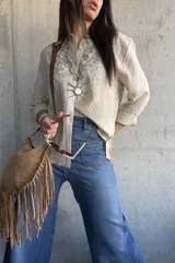 Camisa beige de manga larga con diseño bordado en el pecho, cuello camisero y cierre frontal de botones.
