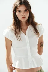 Camisa lisa de algodón blanco, con cuello solapa, manga corta abullonada y bajo en evasé con detalle de peplum. Cierre frontal con botones.
