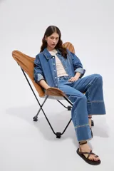 Sobrecamisa de jean azul medio, de corte oversize, con mangas largas y detalles de tachas decorativas en la parte frontal y trasera.