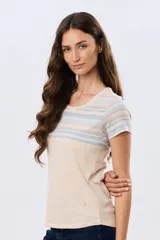 Remera de manga corta con cuello redondo, de color beige con diseño de franjas horizontales en tonos celestes y rosados en la parte superior.