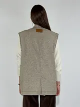 Chaleco largo color crudo con solapas, sin mangas y cierre con dos botones.