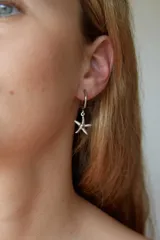 Aros tipo argolla pequeña con dije colgante en forma de estrella de mar, elaborados en acero quirúrgico.