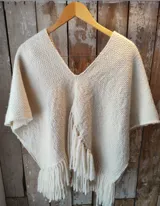 Poncho corto de lana merino color marfil, con escote en V y flecos decorativos en el frente y en el borde inferior.