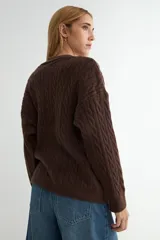 Cardigan de punto con diseño de trenzas, color beige, con escote en V, cierre frontal de botones negros y mangas largas con puños acanalados.