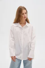 Camisa de algodón blanca, de corte oversize, manga larga y cuello camisero, decorada con apliques de strass y bordados sutiles en la parte delantera.