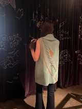 Chaleco verde menta tejido de punto con cuello alto tipo polera, diseño sin mangas, detalles geométricos en tonos tostados y trenza aplicada en la espalda.
