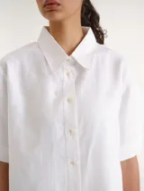 Camisa de manga corta blanca, con cuello camisero, cierre frontal de botones y diseño recto.
