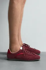 Zapatilla de cordones de estilo retro, con parte superior de serraje color bordó y detalles en piel lisa color rojo. Suela ultrafina de goma en tono marrón oscuro.