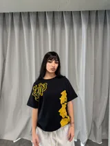 Remera negra de corte regular con estampado gráfico en color amarillo. Presenta inscripciones con estética oriental en la parte superior izquierda y en el lateral derecho. Confeccionada en algodón de alto gramaje con cuello reforzado y grifa de la marca en la manga.
