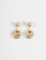 Par de caravanas colgantes doradas con un diseño de doble círculo. El círculo superior es pequeño y liso, mientras que el inferior es más grande, con una forma irregular y un cristal brillante en el centro.