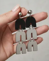 Caravanas colgantes de acero italiano, compuestas por tres piezas articuladas en forma de arco, con acabado bicolor en negro y plateado.
