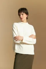Polera de tejido de punto color blanco, con cuello alto acanalado, hombros caídos y detalle de costura vertical en el frente.