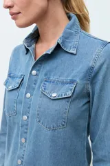 Camisa de jean de corte recto y calce relajado, con cuello clásico, cierre frontal con botones metálicos y dos bolsillos frontales con solapa.