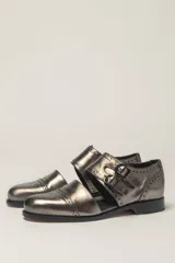 Zapato tipo monk strap con aberturas laterales, confeccionado en cuero vacuno metalizado color bronce. Presenta detalles de perforaciones estilo brogue en la puntera y el talón, y doble hebilla metálica en el empeine.