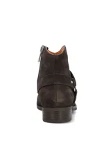 Bota corta de gamuza color marrón oscuro, con punta redonda, taco bajo y cierre lateral. Presenta una tira con tachas metálicas plateadas y una argolla decorativa alrededor del tobillo.