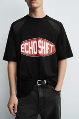 Camiseta negra de corte boxy fit con paneles laterales y de hombros en tejido de malla. Presenta un estampado frontal ovalado con borde rojo y texto blanco que dice "ECHO SHIFT".