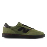 Championes New Balance modelo NM440, color verde oliva con detalles en negro y costuras naranjas. Presentan una silueta de perfil bajo, puntera reforzada y suela de goma negra.