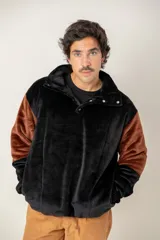 Buzo de textura afelpada en combinación de colores negro y marrón. Presenta cuello camisero con botones a presión, mangas largas y un diseño holgado y confortable.