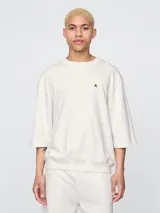 Remera de corte oversized en color beige claro, con cuello redondo y mangas de largo medio. Presenta un pequeño bordado del oso Brannan de Gap en el lado izquierdo del pecho.