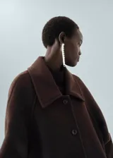 Abrigo largo de lana marrón, diseño recto, con cuello camisero, bolsillos laterales, manga larga y cierre frontal con botones.