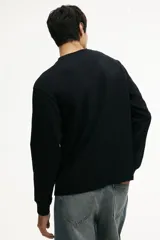 Remera negra de manga larga en punto de algodón de peso medio, con cuello redondo acanalado, hombros caídos, puños acanalados y bajo recto. Presenta un corte holgado.