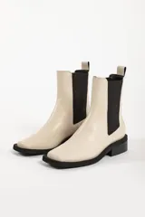 Bota tipo Chelsea de cuero color beige, con paneles laterales elásticos en color negro, puntera cuadrada y suela de goma negra con tacón bajo.