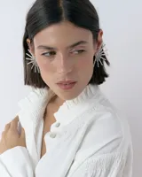 Caravanas tipo ear cuff con diseño de medio sol, compuestas por varillas metálicas plateadas, centro con strass y detalle de resina. Diseño liviano y brillante.