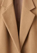 Abrigo de lana color marrón camel, de corte recto y largo midi, con solapas de muesca, bolsillos frontales con solapa y manga larga. Incluye un cinturón fino de cuero oscuro para entallar la cintura.