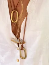 Collar con dije ovalado de bronce colgando de un tiento de cuero marrón.